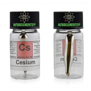 Op de afbeelding: Een doorzichtige glazen fles met een zwarte dop die een klein stukje cesiummetaal bevat. De fles heeft een etiket met de tekst "Cesium Atoomnummer 55" en "NOVAELEMENTS&reg;".