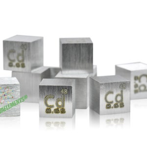 May include: A collection of silver-colored metal cubes, each displaying the chemical symbol "Cd" along with numbers. The cubes are arranged in a group, with some stacked and others scattered. The logo "NOVAELEMENTS" is visible on one cube.