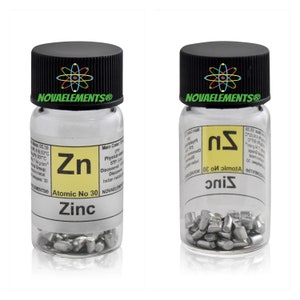 Op de afbeelding: Een klein glazen potje met een zwart deksel dat kleine stukjes zinkmetaal bevat. Het potje heeft een etiket met de tekst "NOVAELEMENTS®" en een periodiek systeem elementvak voor zink met het atoomnummer 30 en de tekst "Zink".