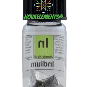 Puede incluir: Una botella de vidrio transparente con una tapa negra que contiene un peque&ntilde;o trozo de metal de Indio. La etiqueta de la botella tiene el s&iacute;mbolo del elemento "In" y el n&uacute;mero at&oacute;mico "49".