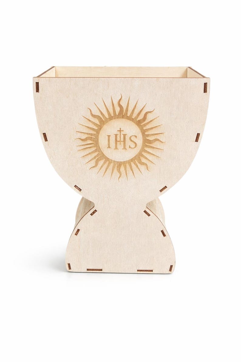 Puede incluir: Una caja de madera de color claro en forma de c&aacute;liz, con un dise&ntilde;o de sol y las letras IHS. La caja tiene una parte superior cuadrada y una base redondeada, con ranuras para el montaje. Decoraci&oacute;n de tem&aacute;tica religiosa.