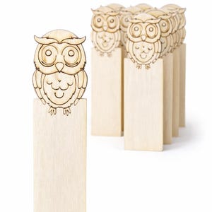 Könnte beinhalten: Lesezeichen aus Holz in Eulenform. Jedes Lesezeichen hat ein lasergeschnittenes Eulen-Design auf einer rechteckigen Basis. Die Eulen haben große Augen und einen lächelnden Ausdruck. Das Holz hat eine natürliche, helle Farbe.