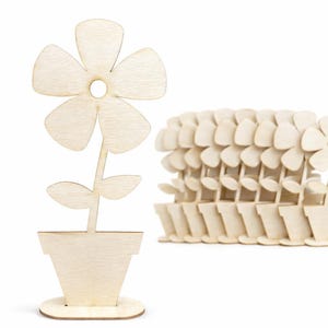 May include: Wooden flower decorations. One flower is fully assembled, while a stack of others are in a row. The flowers are in a pot with a round base. The flowers have five petals and two leaves.
