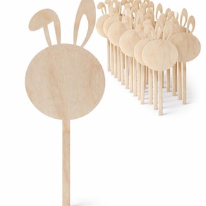 Puede incluir: Un conjunto de adornos de madera con forma de conejito. Cada adorno tiene un cuerpo redondo, orejas de conejo y un palito. La madera es de color claro natural. Ideales para decoraciones de Pascua o primavera.