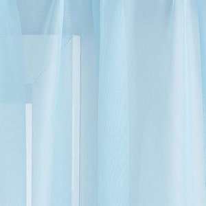 May include: A sheer light blue curtain panel hangs in a window. The curtain is made of a lightweight fabric that allows light to filter through.