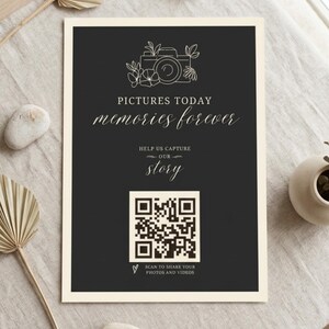 May include: A rectangular sign with a dark gray background and cream border. It features a line-art camera icon, the text "PICTURES TODAY memories forever", "HELP US CAPTURE OUR story", a central QR code, and "SCAN TO SHARE YOUR PHOTOS AND VIDEOS".