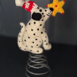 Può includere: Una stravagante statuetta di cane dalmata con macchie nere, che indossa un cappello a maglia rosso e bianco. Il cane tiene in mano una stella gialla con dettagli rossi. La statuetta è montata su una base a molla argentata, perfetta per le decorazioni natalizie.