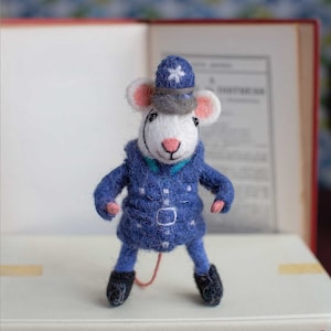 Peut inclure: Une souris en feutre blanc portant un uniforme de policier bleu avec un chapeau gris et une étoile blanche. La souris est debout sur un livre avec le texte "JIM AT THE CORNER - Eleanor Farjeon" sur la couverture.