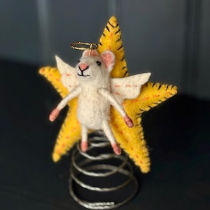 May include: A charming felt mouse angel figurine with white fur, pink ears and feet, and small white wings. The mouse is perched on a yellow star with black stitching, and a gold halo. The star sits atop a silver metal spring.