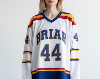 May include: A white long-sleeve hockey jersey featuring the word BRIAR in blue letters above the number 44 in blue with yellow outlines. The sleeves and hem have blue, yellow, and red horizontal stripes. The number 4 is on each shoulder.
