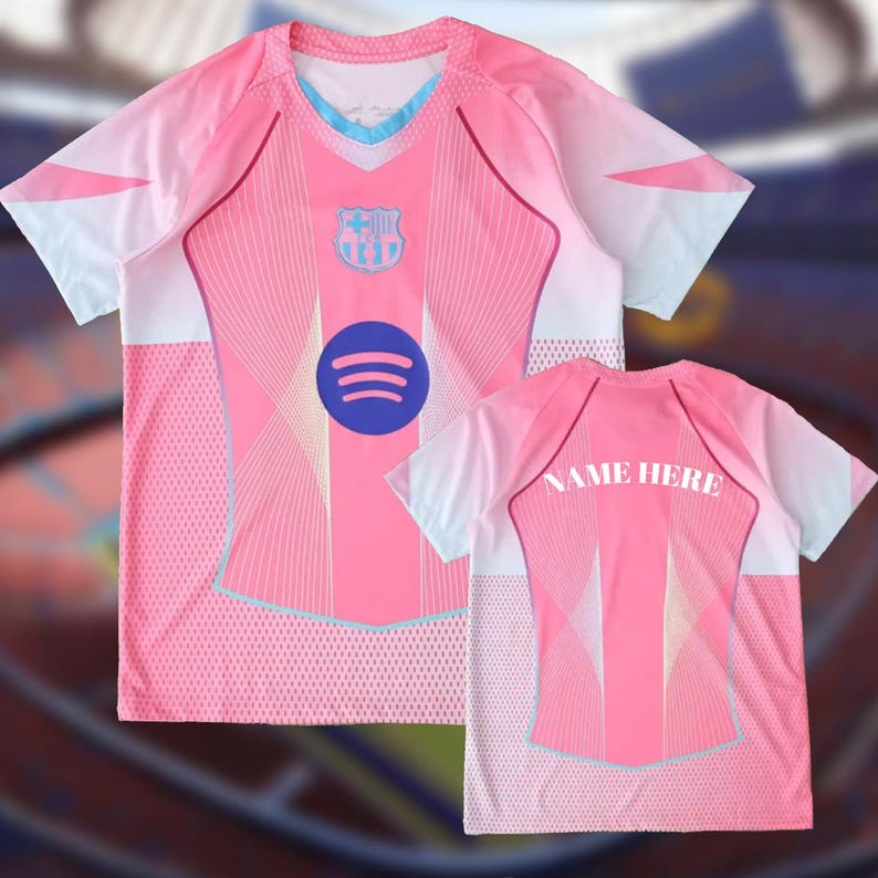 K&ouml;nnte beinhalten: Rosa-wei&szlig;es Fu&szlig;balltrikot mit blauem Spotify-Logo und Teamwappen. Das Trikot hat ein geometrisches Design und den Text "NAME HERE" auf der R&uuml;ckseite. Es hat kurze &Auml;rmel und einen Rundhalsausschnitt.