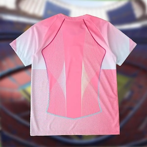 K&ouml;nnte beinhalten: Ein pinkfarbenes Sportshirt mit Farbverlauf. Das Shirt hat wei&szlig;e und rosa &Auml;rmel, ein Mesh-Panel an den Seiten und ein geometrisches Muster auf dem R&uuml;cken. Das Shirt hat einen Rundhalsausschnitt und kurze &Auml;rmel.