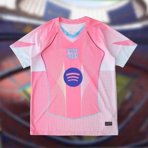 K&ouml;nnte beinhalten: Rosa Fu&szlig;balltrikot mit V-Ausschnitt und kurzen &Auml;rmeln. Das Trikot hat ein Teamwappen und ein Spotify-Logo auf der Vorderseite. Das Design umfasst hellblaue und wei&szlig;e Akzente.