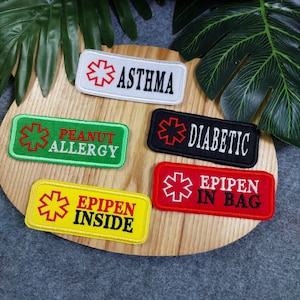 May include: Five embroidered patches with red medical symbols and text. The patches are on a wooden surface. The patches read "Asthma", "Peanut Allergy", "Diabetic", "EpiPen Inside", and "EpiPen In Bag".