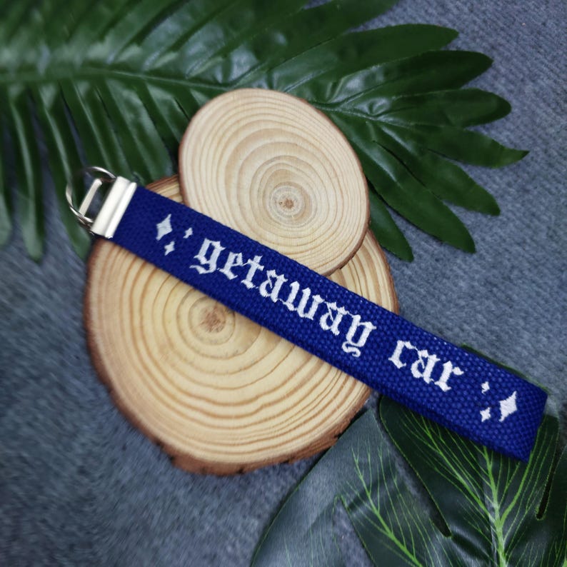 May include: Blue key chain with white text that reads "getaway car" in old English font. The key chain has a silver metal ring.
