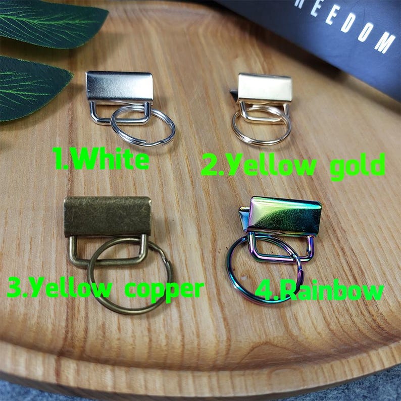 May include: Four keychains with different finishes: white, yellow gold, yellow copper, and rainbow. Each keychain has a metal ring attached.