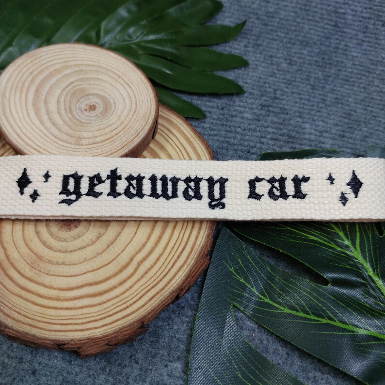 May include: A white cotton webbing keychain with black embroidered text that reads "getaway car" with diamond symbols on either side.