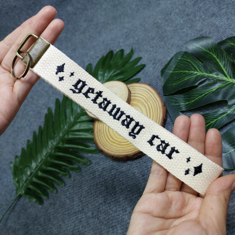 May include: White canvas keychain with black embroidered text that reads "getaway car" with a diamond symbol on each end.