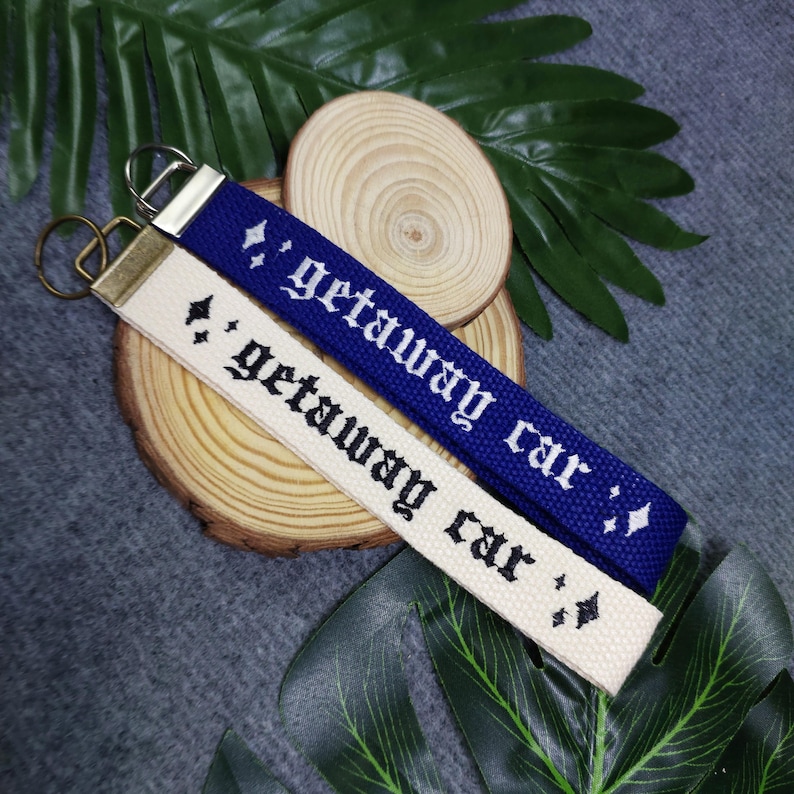 May include: Two keychains with the text "getaway car" embroidered on them. One keychain is white with black embroidery and the other is blue with white embroidery.