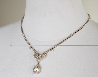 May include: A silver necklace with a teardrop-shaped pendant set with clear rhinestones.