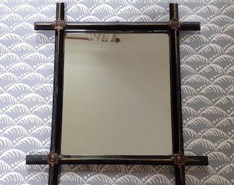 May include: A black framed mirror with ornate gold accents and a simple, rectangular shape. The mirror is hanging on a wall with a white and gray patterned wallpaper.