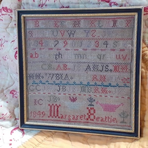 以下が含まれることがあります： 黒と金のフレームに入ったサンプラー。サンプラーはリネン製で、クロスステッチ、サテンステッチ、フレンチノットなど、さまざまなステッチが施されています。サンプラーにはアルファベット、数字、1849年の日付が記されています。サンプラーには「マーガレット・ビーティ」の署名があります。