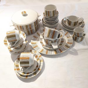 May include: A complete vintage dinnerware set with a white background. The set includes cups, saucers, plates, a serving bowl, and a creamer. The pieces feature a pattern of brown, gold, and black horizontal lines.