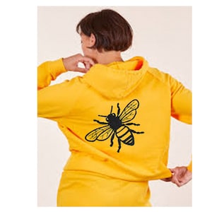 Op de afbeelding: Een gele hoodie met een zwart bijenontwerp op de rug. De bij is gedetailleerd met zwarte vleugels en gele strepen.