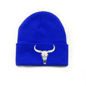 Op de afbeelding: Koningsblauwe beanie met een witte schedel van een stier. De schedel met grote hoorns is gecentreerd op de omgevouwen rand van de muts. De beanie is gemaakt van een zacht, gebreid materiaal.