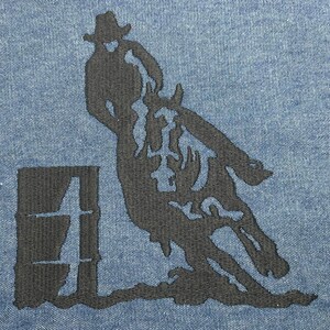 Op de afbeelding: Zwarte silhouet van een persoon die een paard over een vat rijdt, geborduurd op een blauwe denim stof.