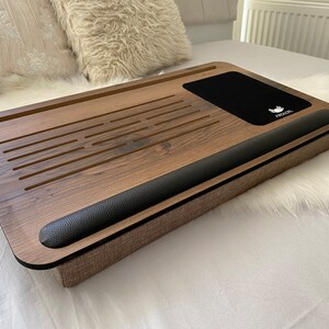 Może przedstawiać: Drewniany stojak na laptopa z czarnym sk&oacute;rzanym podłokietnikiem i czarną poduszką z tkaniny. Stojak ma wbudowaną podkładkę pod mysz z nadrukowanym słowem "MOUSE".