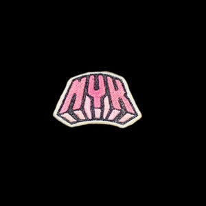 May include: An embroidered patch featuring the letters NYK in a bold, stylised pink font with a dark outline. The design has a trapezoidal shape with a light-coloured border, showcasing detailed stitching throughout the entire graphic element.