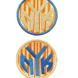 Puede incluir: Dos parches bordados circulares con las letras NYK en el centro. El parche superior tiene letras beige sobre un fondo de rayas naranjas y blancas con un borde azul. El parche inferior tiene letras azules sobre un fondo de rayas naranjas y blancas con un borde naranja claro.