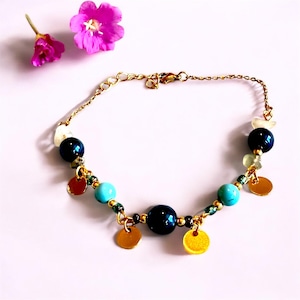 May include: A gold-toned bracelet featuring a variety of beads in teal, navy, and white, interspersed with small gold-colored disc charms. The bracelet is accented with small green beads and a delicate chain.