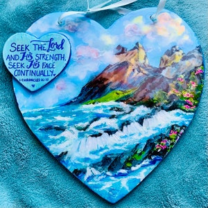 May include: A heart-shaped painting depicting a blue and white ocean scene, a mountain range in the background, and a sky with clouds. The painting features the text "Seek the Lord and His strength, Seek His face continually. 1 Chronicles 16:11" written on it.