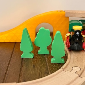 May include: A toy train engine with a black body, red wheels, and a yellow whistle travels on a wooden track with green trees. The train is going under a wooden bridge.