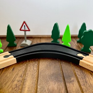 May include: A black wooden train track with a curved section. The track is on a wooden surface with green and brown wooden trees and a red and white warning sign.