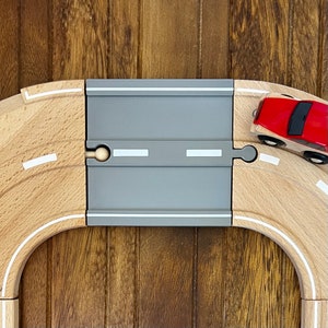 May include: A wooden toy race track with a gray road and a red toy car driving on it.