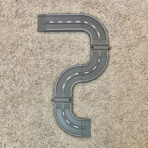 May include: A gray plastic toy race track with a curved design. The track is made up of multiple pieces that connect together to form a continuous loop.
