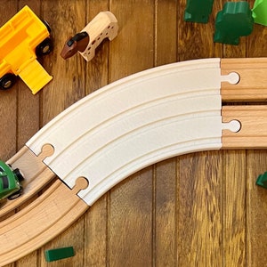 Puede incluir: Un set de vías de tren de juguete de madera con una pieza de vía curva blanca y dos piezas de vía de madera marrón. Las piezas de vía se conectan entre sí con un diseño de enclavamiento simple.