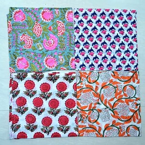 May include: Four cotton napkins with floral patterns. The napkins are white with different colored floral designs. One napkin has a blue background with pink flowers, another has a white background with red flowers, another has a white background with orange flowers, and the last one has a white background with pink and blue flowers.