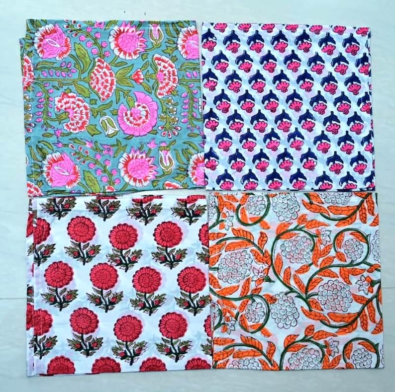 May include: Four cotton napkins with floral patterns. The napkins are white with different colored floral designs. One napkin has a blue background with pink flowers, another has a white background with red flowers, another has a white background with orange flowers, and the last one has a white background with pink and blue flowers.