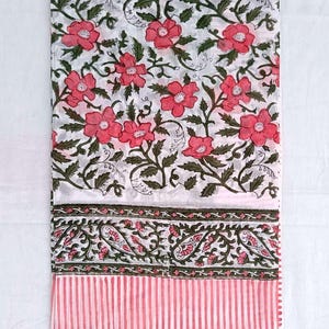 May include: White textile with a floral design of pink flowers and green leaves. The fabric has a border with paisley and pink vertical stripes. The textile is folded and displayed on a white surface.