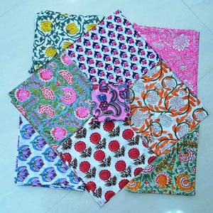 May include: A set of eight colorful cotton napkins with floral patterns. The napkins are folded and arranged in a circular pattern. The napkins are in various colors, including pink, blue, green, and orange.