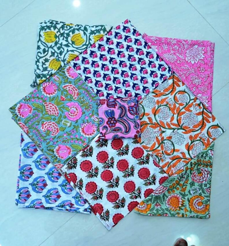 May include: A set of eight colorful cotton napkins with floral patterns. The napkins are folded and arranged in a circular pattern. The napkins are in various colors, including pink, blue, green, and orange.