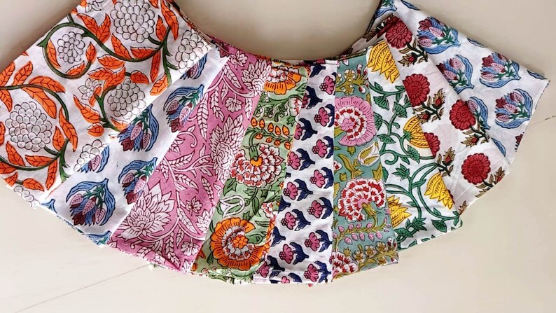 May include: A set of eight fabric squares with floral patterns in various colors, including pink, green, blue, orange, and white. The fabric squares are arranged in a fan shape.
