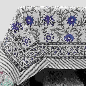 Puede incluir: Un mantel blanco con un estampado floral con flores azules y vides grises. El borde tiene un diseño a rayas en gris y blanco. El mantel está hecho de un material suave, probablemente algodón.