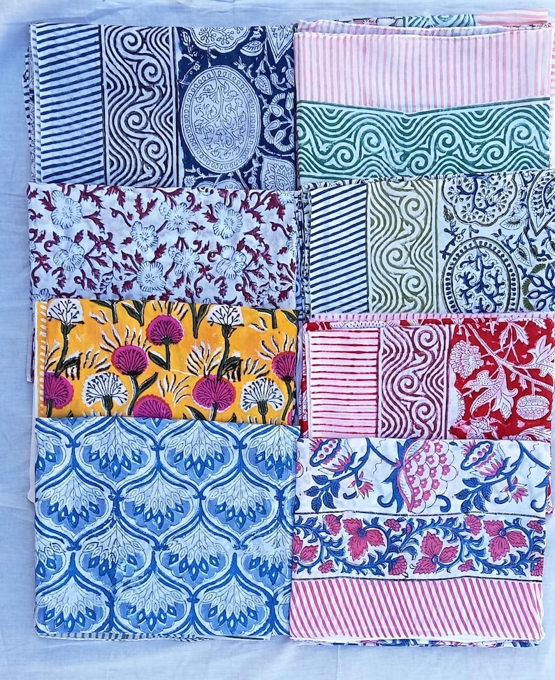 May include: A selection of folded fabric pieces with diverse patterns. Designs include stripes, swirls, floral, and geometric shapes in colours like blue, red, yellow, and green. The fabrics appear to be cotton or a similar material.
