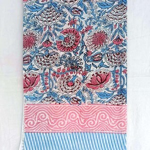 May include: A folded textile with a floral design in pink and blue on a white backdrop. The pattern showcases large flowers and leaves. The lower section has a pink wavy pattern and blue stripes.