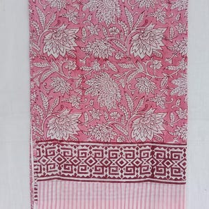 May include: Pink floral fabric featuring a white floral design. The fabric has a border with geometric shapes in a darker pink and a striped pattern. Suitable for home decor or clothing, the fabric is likely cotton or linen.